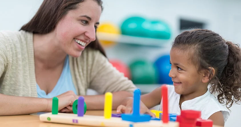 An occupational therapist playing a stacking game with a young girl